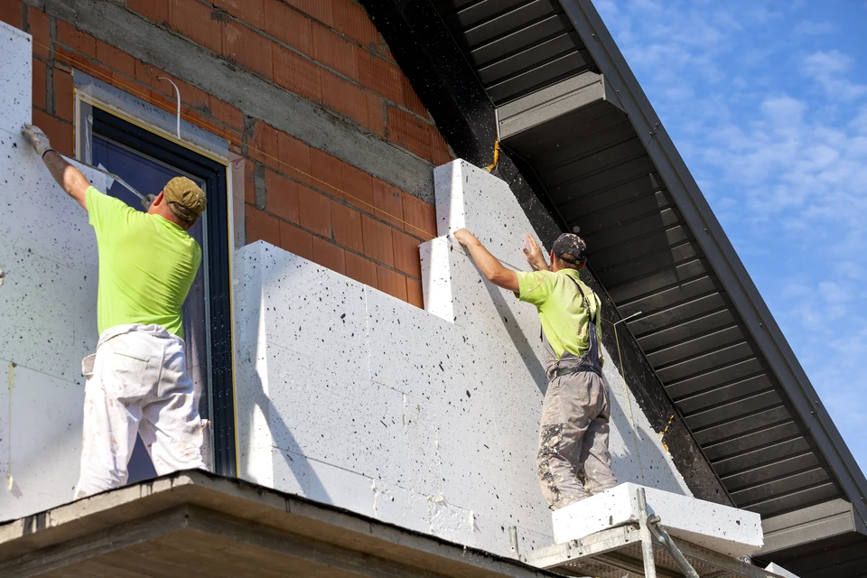 Deux ouvriers en vêtements haute visibilité installent des panneaux d'isolation thermique extérieure sur façade de maison individuelle